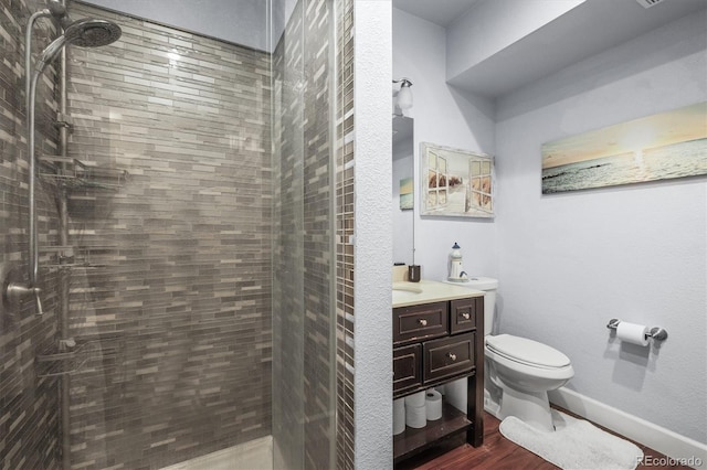 full bathroom featuring toilet, tiled shower, vanity, wood finished floors, and baseboards