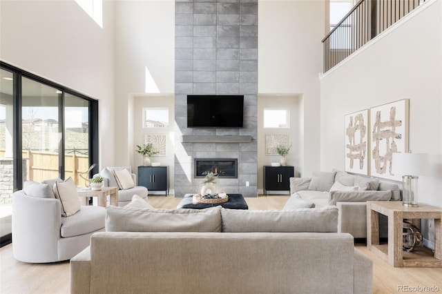 living room with a high ceiling, a tiled fireplace, and light wood finished floors