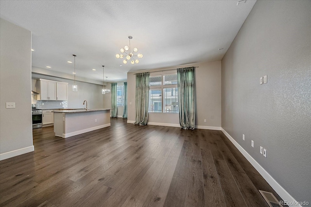 unfurnished living room featuring an inviting chandelier, sink, and dark wood-type flooring