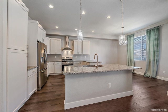 kitchen with pendant lighting, sink, a kitchen island with sink, stainless steel appliances, and wall chimney range hood