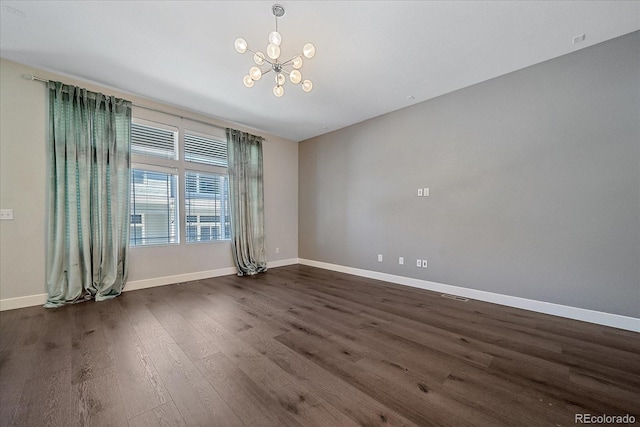 spare room featuring dark wood-type flooring and a notable chandelier