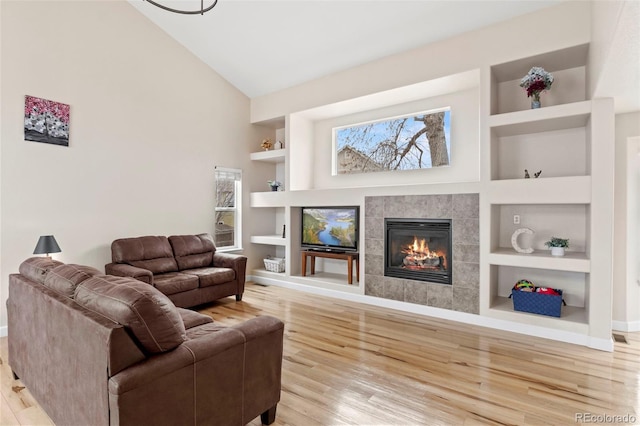 4426 Crow Creek Dr, Colorado Springs, CO 80922 - living room with built in shelves, a tile fireplace, light wood-style floors, baseboards, and high vaulted ceiling
