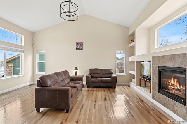 4426 Crow Creek Dr, Colorado Springs, CO 80922 - living area featuring light wood-style flooring, a tiled fireplace, a chandelier, baseboards, and high vaulted ceiling