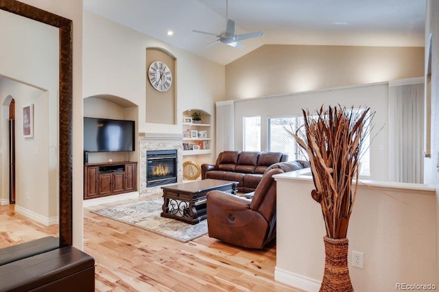 living room featuring ceiling fan, light wood-type flooring, a fireplace, and high vaulted ceiling