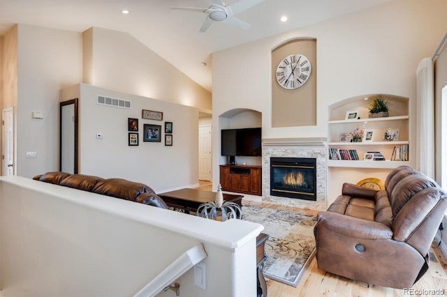 living room with ceiling fan, light hardwood / wood-style flooring, high vaulted ceiling, and built in features