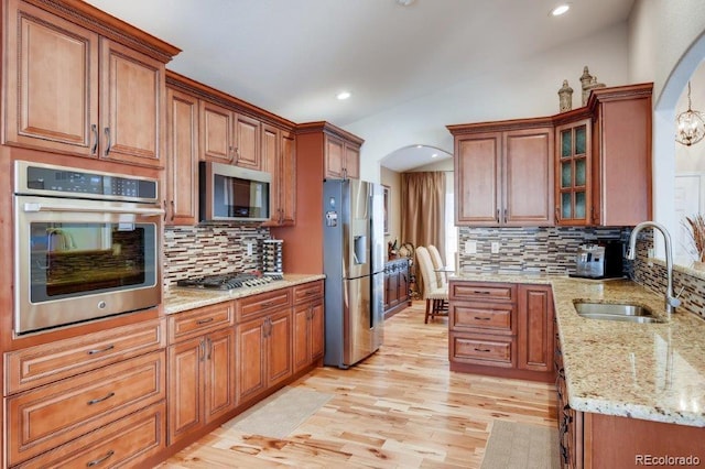 kitchen with light stone countertops, sink, light hardwood / wood-style floors, decorative backsplash, and appliances with stainless steel finishes