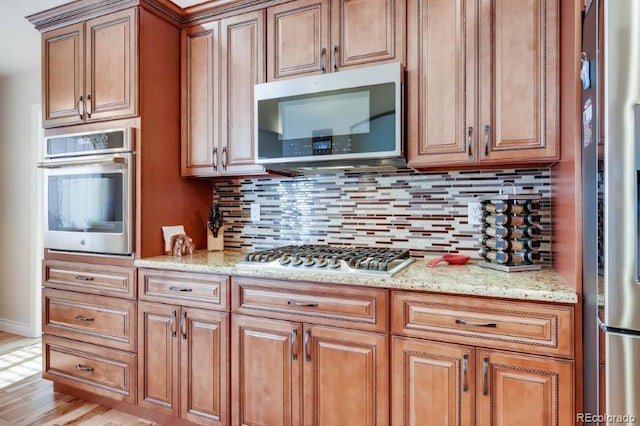 kitchen with backsplash, light stone counters, stainless steel appliances, and light hardwood / wood-style flooring