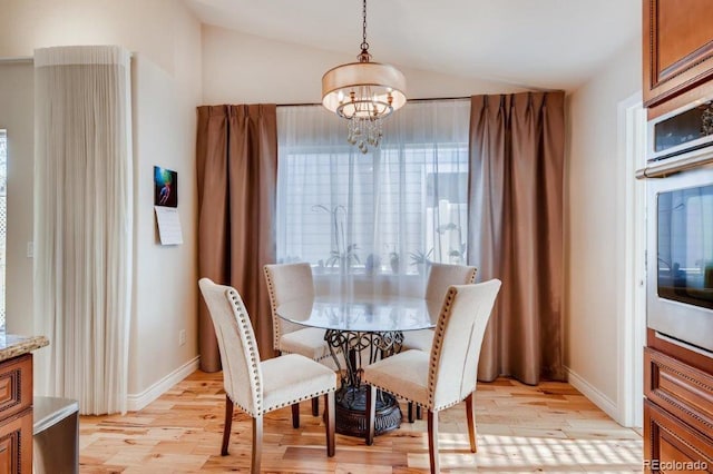 dining area featuring a chandelier, light wood-type flooring, and vaulted ceiling