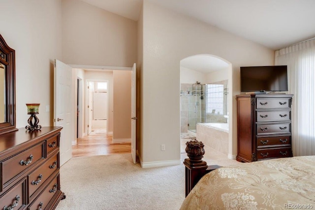 bedroom featuring ensuite bath, light carpet, and lofted ceiling