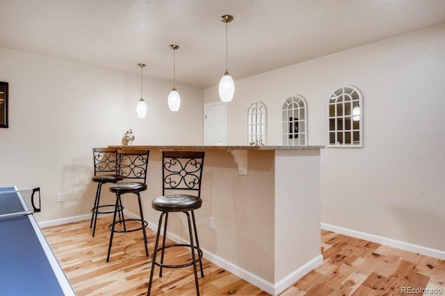 kitchen with kitchen peninsula, pendant lighting, light hardwood / wood-style flooring, and a breakfast bar area