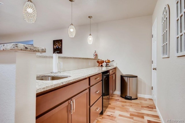 kitchen with light stone countertops, pendant lighting, light wood-type flooring, and sink