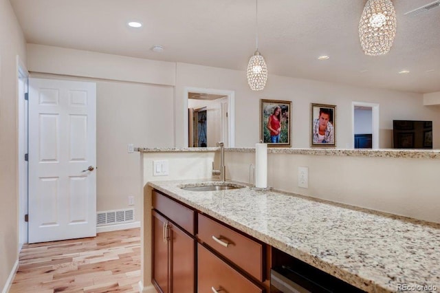 kitchen featuring light stone countertops, light wood-type flooring, sink, and hanging light fixtures