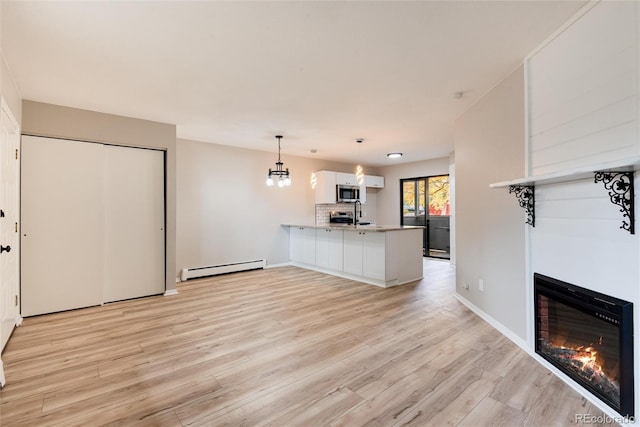 unfurnished living room featuring a chandelier, baseboard heating, and light hardwood / wood-style flooring