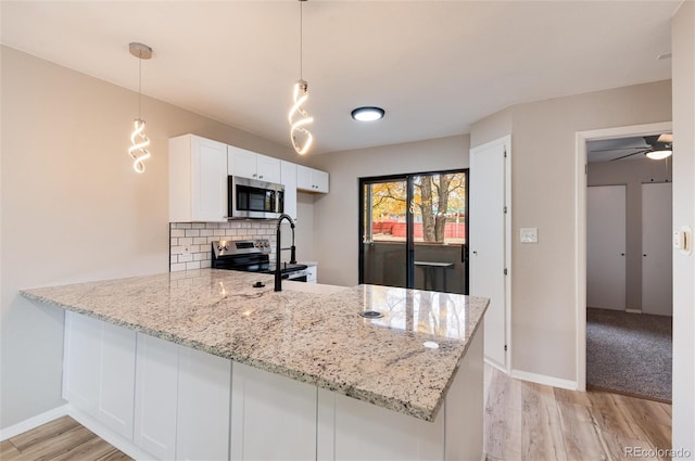 kitchen with appliances with stainless steel finishes, a peninsula, light wood-style floors, and light stone countertops