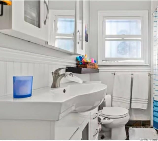 bathroom featuring a wainscoted wall, toilet, a shower with shower curtain, and vanity