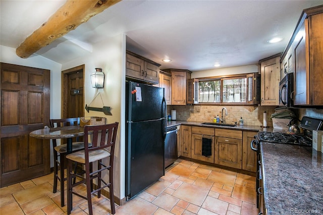 kitchen with decorative backsplash, sink, black appliances, beam ceiling, and dark stone countertops