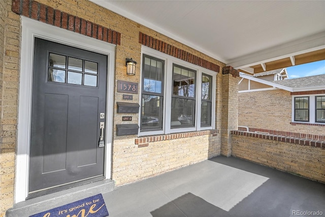 property entrance featuring covered porch and brick siding