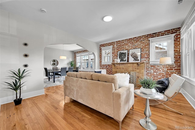 living area featuring light wood-style floors, arched walkways, baseboards, and brick wall