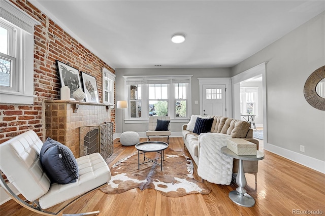 living room with a brick fireplace, baseboards, wood finished floors, and brick wall