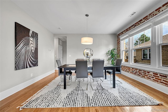 dining space featuring brick wall, baseboards, wood finished floors, and visible vents