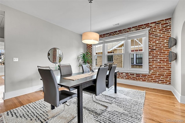 dining area with baseboards, light wood-style floors, brick wall, and visible vents