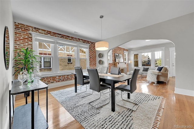 dining room with arched walkways, baseboards, brick wall, and wood finished floors