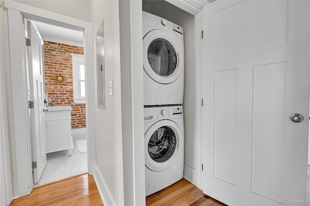 clothes washing area with stacked washing maching and dryer, laundry area, light wood-type flooring, and brick wall