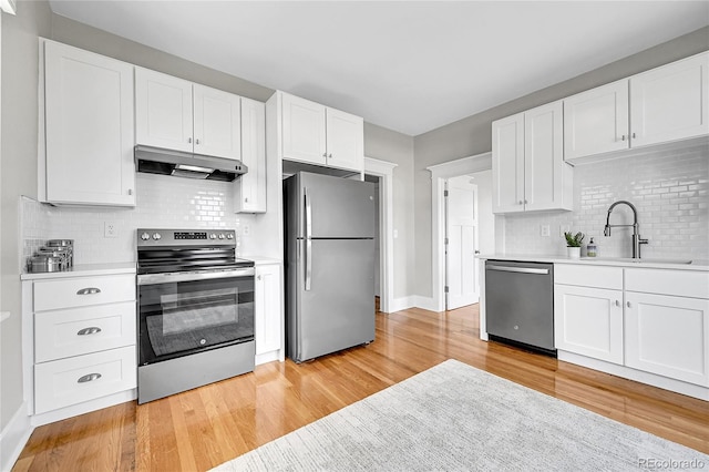 kitchen with appliances with stainless steel finishes, light wood finished floors, light countertops, backsplash, and under cabinet range hood