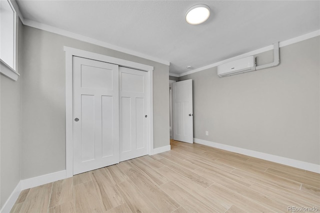 unfurnished bedroom with crown molding, an AC wall unit, light wood-style flooring, baseboards, and a closet