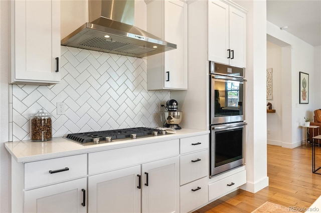 2027 Vallejo Loop, Broomfield, CO 80023 - kitchen featuring wall chimney exhaust hood, appliances with stainless steel finishes, decorative backsplash, light countertops, and light wood-style floors