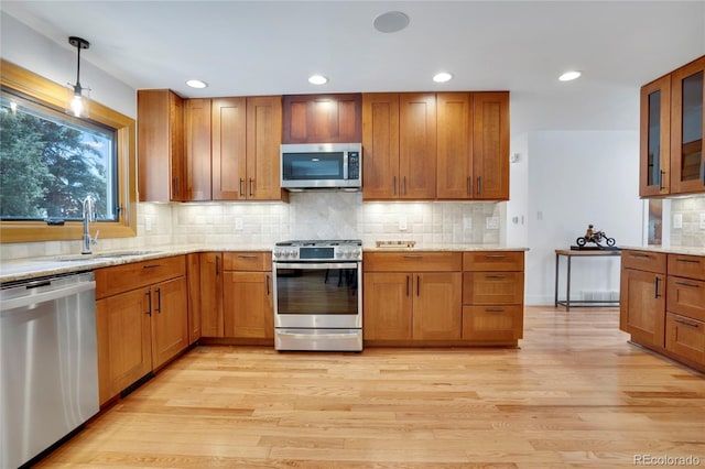 kitchen featuring a sink, stainless steel appliances, brown cabinets, light wood finished floors, and backsplash