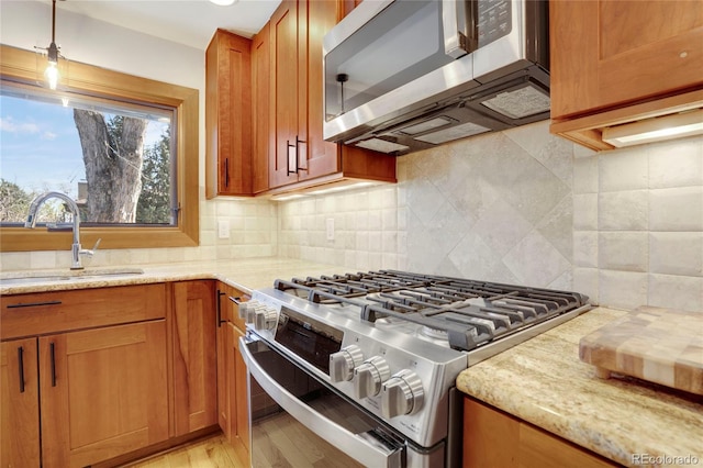 kitchen with appliances with stainless steel finishes, a sink, backsplash, and light stone countertops