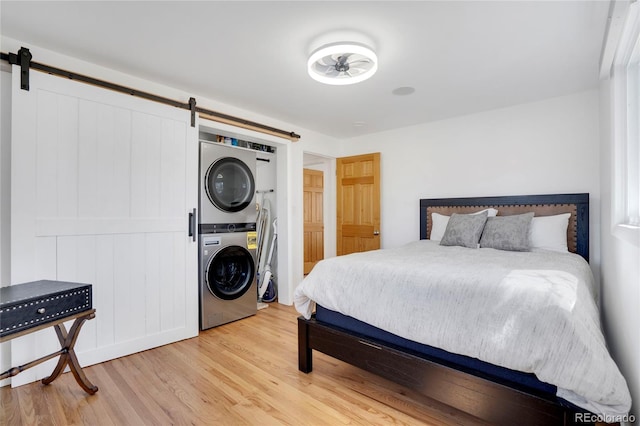 bedroom with a barn door, wood finished floors, and stacked washer and clothes dryer