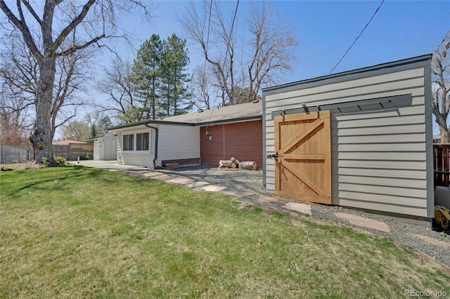 rear view of property with an outbuilding, a yard, a storage unit, fence, and brick siding