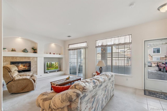 living area featuring built in features, light colored carpet, visible vents, a tiled fireplace, and light tile patterned flooring