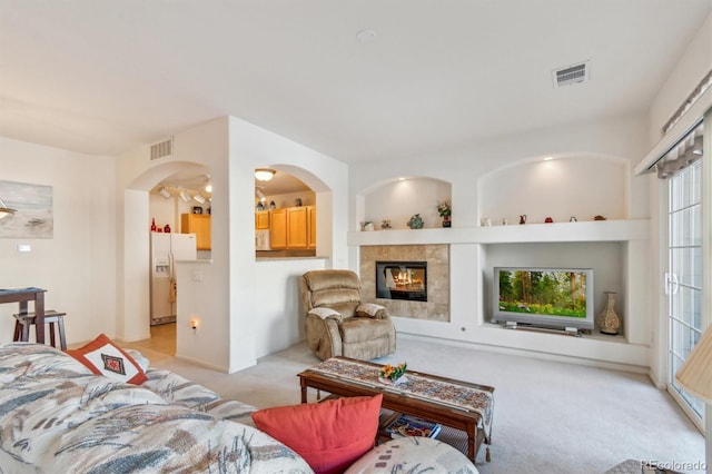 living area with built in shelves, a tiled fireplace, visible vents, and light colored carpet