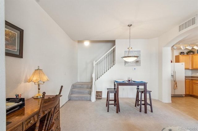 dining area with light carpet, stairs, visible vents, and arched walkways