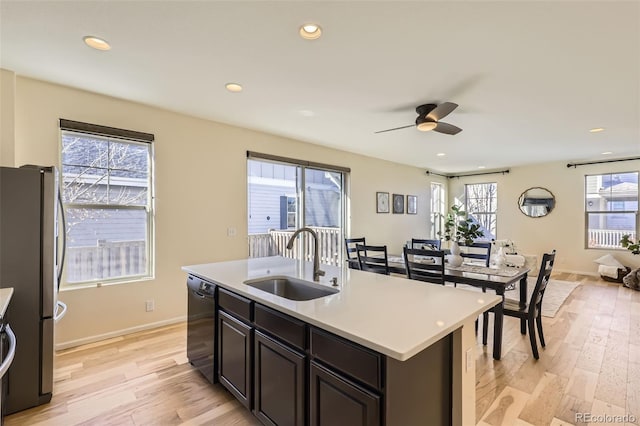 kitchen with stainless steel refrigerator, black dishwasher, sink, light hardwood / wood-style floors, and a center island with sink