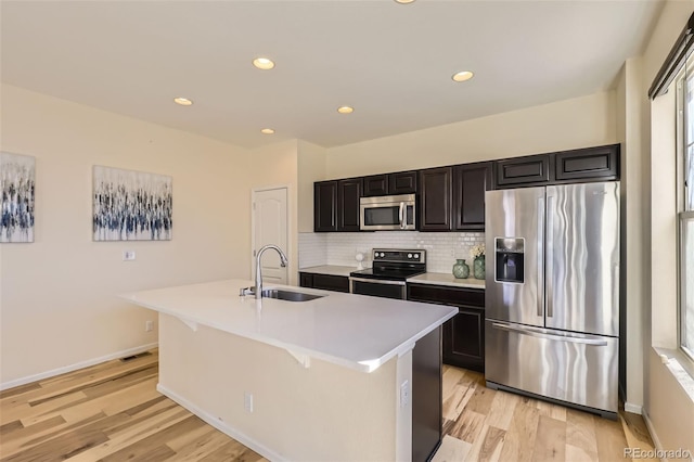 kitchen featuring light countertops, appliances with stainless steel finishes, a sink, an island with sink, and light wood-type flooring