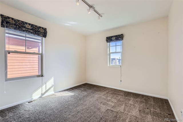 unfurnished room with baseboards, track lighting, visible vents, and carpet flooring