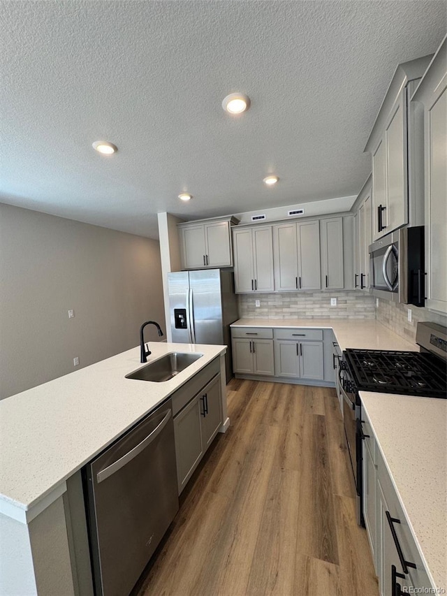 kitchen with appliances with stainless steel finishes, wood finished floors, light stone countertops, gray cabinets, and a sink