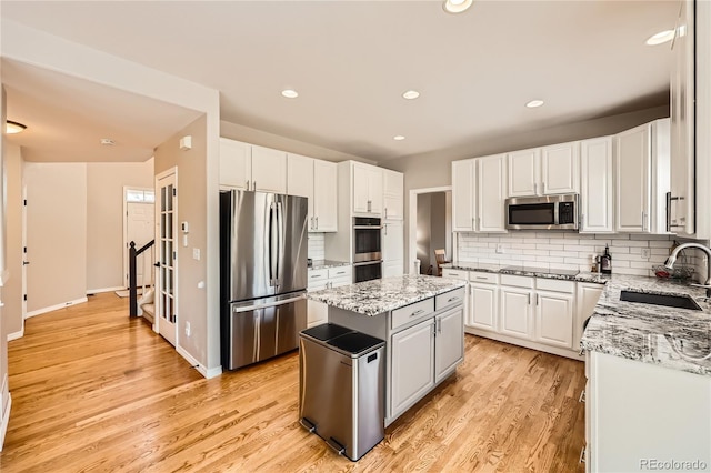 kitchen featuring decorative backsplash, appliances with stainless steel finishes, a sink, a kitchen island, and light wood-type flooring