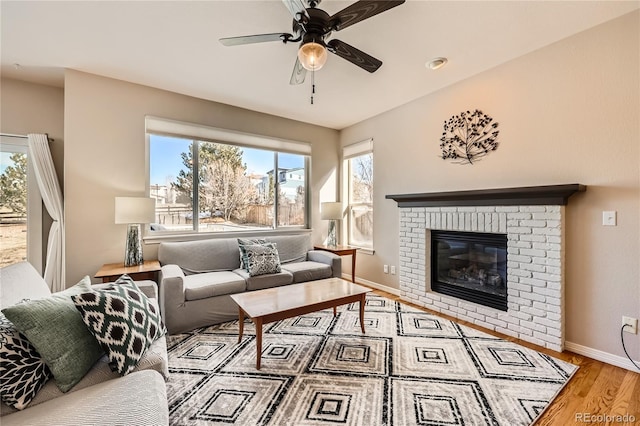 living area featuring ceiling fan, a fireplace, baseboards, and wood finished floors