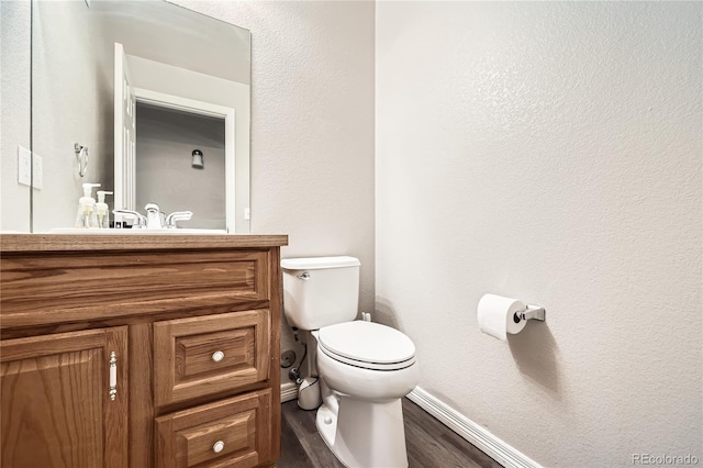 bathroom with a textured wall, toilet, wood finished floors, vanity, and baseboards