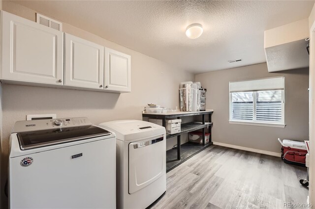 washroom featuring a textured ceiling, baseboards, light wood-style floors, washer and dryer, and cabinet space