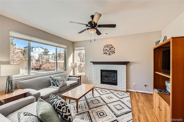 living room featuring light wood-style floors, baseboards, a ceiling fan, and a brick fireplace