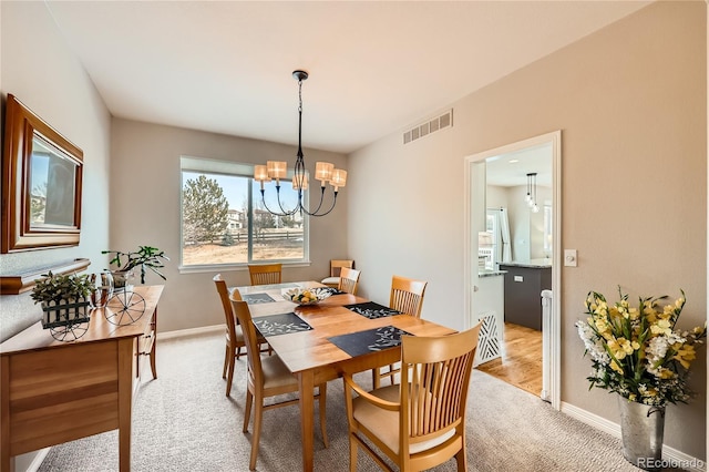dining room with light carpet, a notable chandelier, visible vents, and baseboards