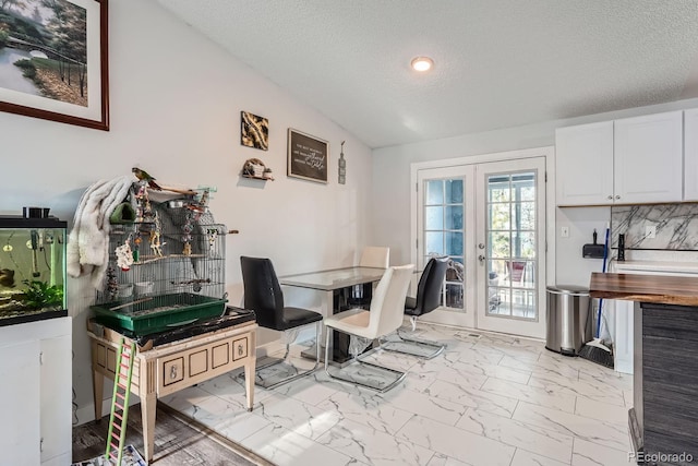 dining room featuring vaulted ceiling, marble finish floor, french doors, and a textured ceiling