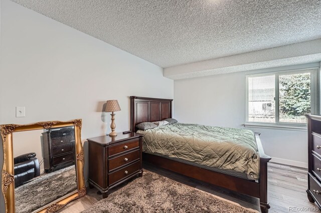 bedroom featuring a textured ceiling, baseboards, and wood finished floors