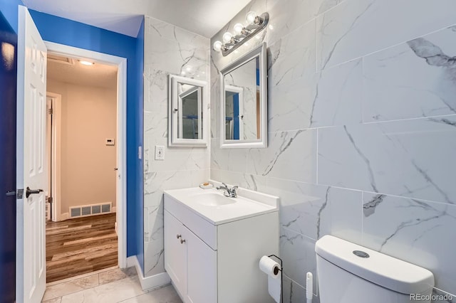 half bath with toilet, vanity, visible vents, and tile walls